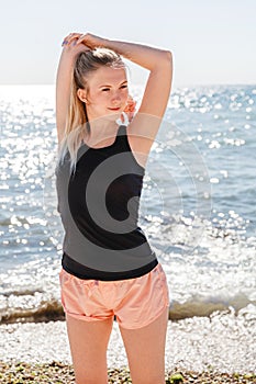 A blonde girl in a dark t shirt and light shorts does sports in the summer on the sea coast