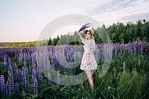 A blonde girl in a dress straw hat holding a bouquet of lupins