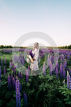 A blonde girl in a dress straw hat holding a bouquet of lupins