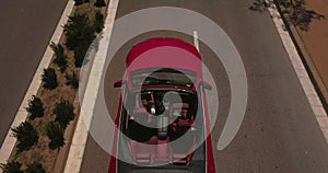 A blonde girl driving a red convertible is driving. Shooting from above using a drone