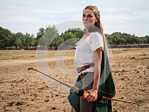 Blonde girl with elf ears poses in the field with a bow and a green cape