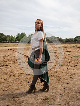 Blonde girl with elf ears poses in the field with a bow and a green cape