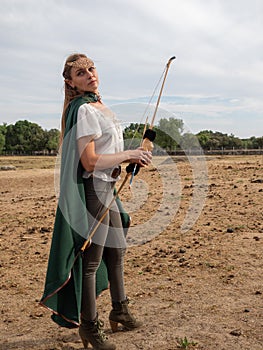 Blonde girl with elf ears poses in the field with a bow and a green cape