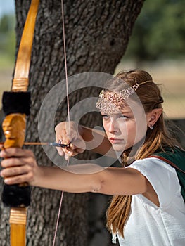 Blonde girl with elf ears poses in the field with a bow and a green cape