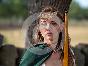 Blonde girl with elf ears poses in the field with a bow and a green cape
