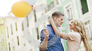 Blonde girl embracing beloved young man, couple dating, holding balloons