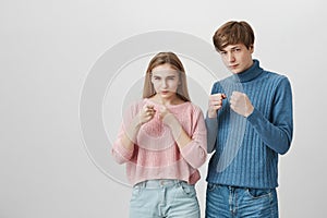 Blonde girl and fair-haired guy standing indoors with fists bunched and determined face expressions. Caucasian young