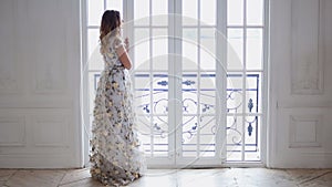 Blonde girl fits a big window in a bright long dress