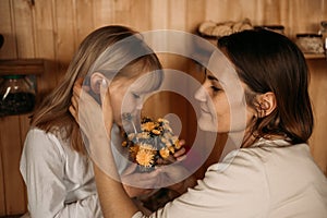 Blonde girl gives mom flowers for mother`s day. Mom and daughter are considering a bouquet of dandelions