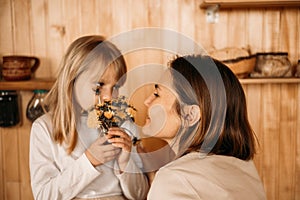 Blonde girl gives mom flowers for mother`s day. Mom and daughter are considering a bouquet of dandelions