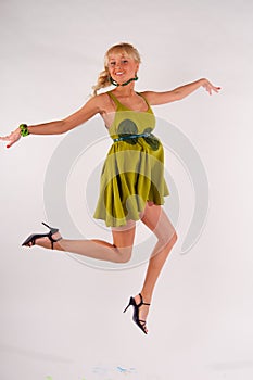 Blonde girl in a green dress jumping in the studio on a white background