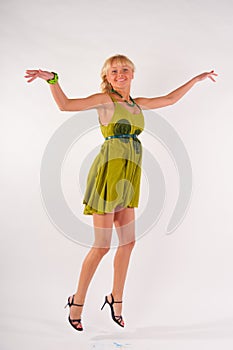 Blonde girl in a green dress jumping in the studio on a white background