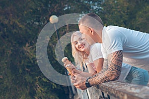 Blonde girl and a guy are standing with ice cream and smiling in the park