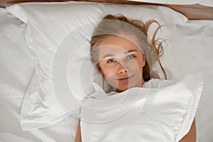 Blonde girl holding pillow in bed.