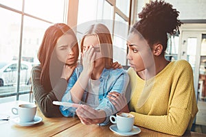 Blonde girl is holding a pregnancy test that shows to her positive result of the test. She looks dissapointed, sad and