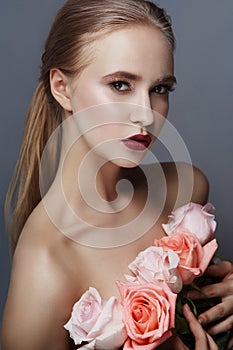 Blonde girl holding rose flowers near her face. Beauty portrait of a woman on a dark background. Perfect makeup, beautiful body