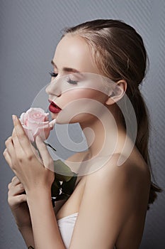 Blonde girl holding rose flowers near her face. Beauty portrait of a woman on a dark background. Perfect makeup, beautiful body