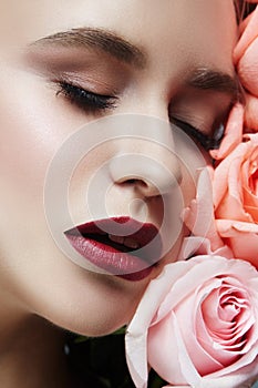 Blonde girl holding rose flowers near her face. Beauty portrait of a woman on a dark background. Perfect makeup, beautiful body