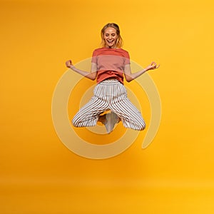 Blonde girl jumps in yogas position. Relax concept. Yellow background