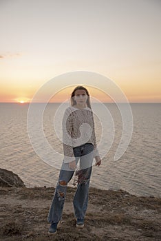 A blonde girl in leaky jeans poses against the background of the sunset