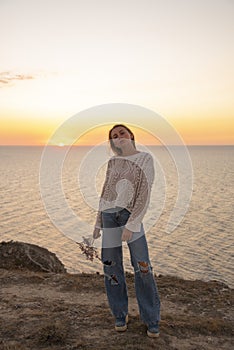 A blonde girl in leaky jeans poses against the background of the sunset