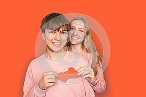 Blonde girl with long hair and brown-haired guy are holding two red hearts in their hands, symbol of love. Red background