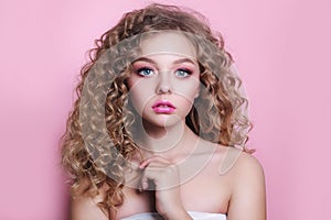 Blonde girl with long and shiny curly hair . Beautiful model woman with wavy hairstyle on pink background