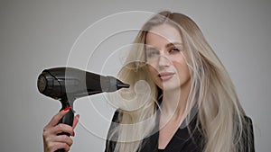 Blonde girl with long straight hair dries her hair with a hair dryer