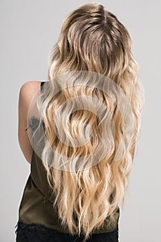 Blonde girl with long and volume shiny wavy hair.