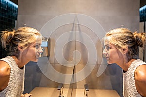 Blonde girl looking at herself in the mirror with her image reflected