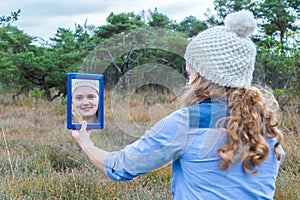 Blonde girl looking in mirror with forest background