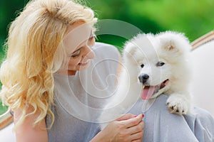 Blonde girl is lying outdoors with a white dog in hands