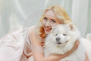 Blonde girl is lying outdoors with a white dog in hands