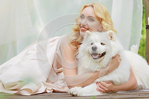 Blonde girl is lying outdoors with a white dog in hands