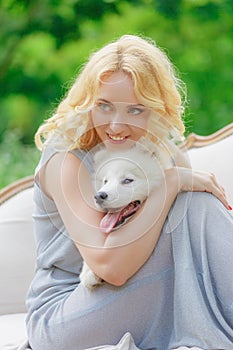 Blonde girl is lying outdoors with a white dog in hands