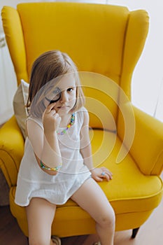 Blonde girl with a magnifying glass in her eye sitting on a yellow armchair