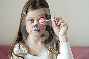 Blonde girl with a make-up imitating a cat holds in her hand a chupa chups.