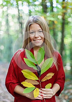 Blonde girl in a misterious forest holding a branch with autumn