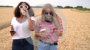 Blonde girl and mixed race teenager drinking coffee and taking selfies on their smart phones for social media