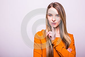 Blonde girl in orange t-shirt with silence gesture on white