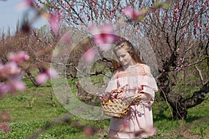 Blonde girl in pink dress is collecting flowers in the garden
