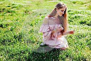 Blonde girl in pink dress is collecting flowers in the garden