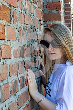 Blonde girl posing near brick wall, sensual beauty face, dark glasses