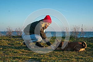A blonde girl with a purebred dog from the shelter. Playing with a dog on the seashore. Friendship of a dog and a person