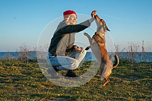 A blonde girl with a purebred dog from the shelter. Playing with a dog on the seashore. Friendship of a dog and a person