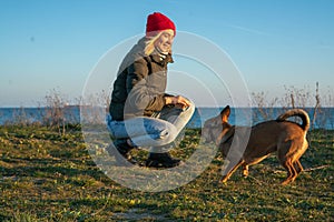 A blonde girl with a purebred dog from the shelter. Playing with a dog on the seashore. Friendship of a dog and a person