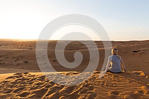 Blonde girl relaxes at sunset in Wahiba sands, Oman