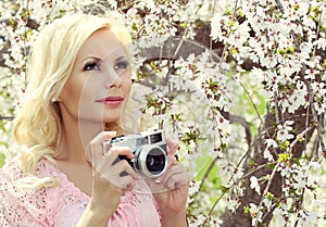 Blonde Girl with Retro Camera over Sakura. Beautiful Young Woman