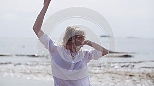 Blonde girl sensually dancing on a background of the sea in white and black clothes