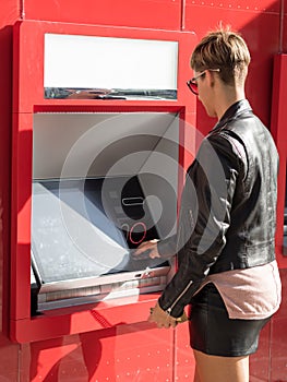 Blonde girl with short hair and dressed in black leather, taking out money at an ATM